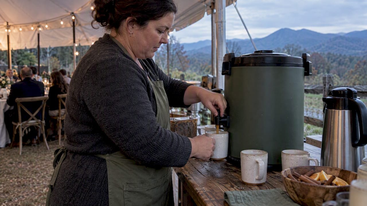 Host pouring warm cider at wedding station